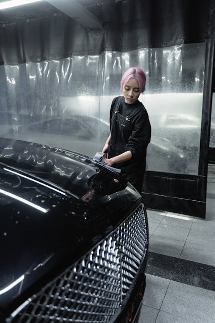 Asian woman with dyed hair detailing a black car at a car wash facility indoors.